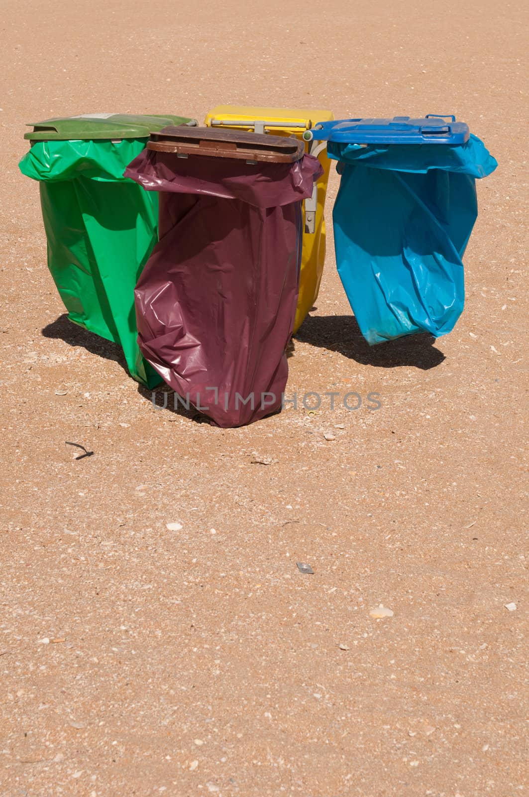 four colorful recycle bins on a beach