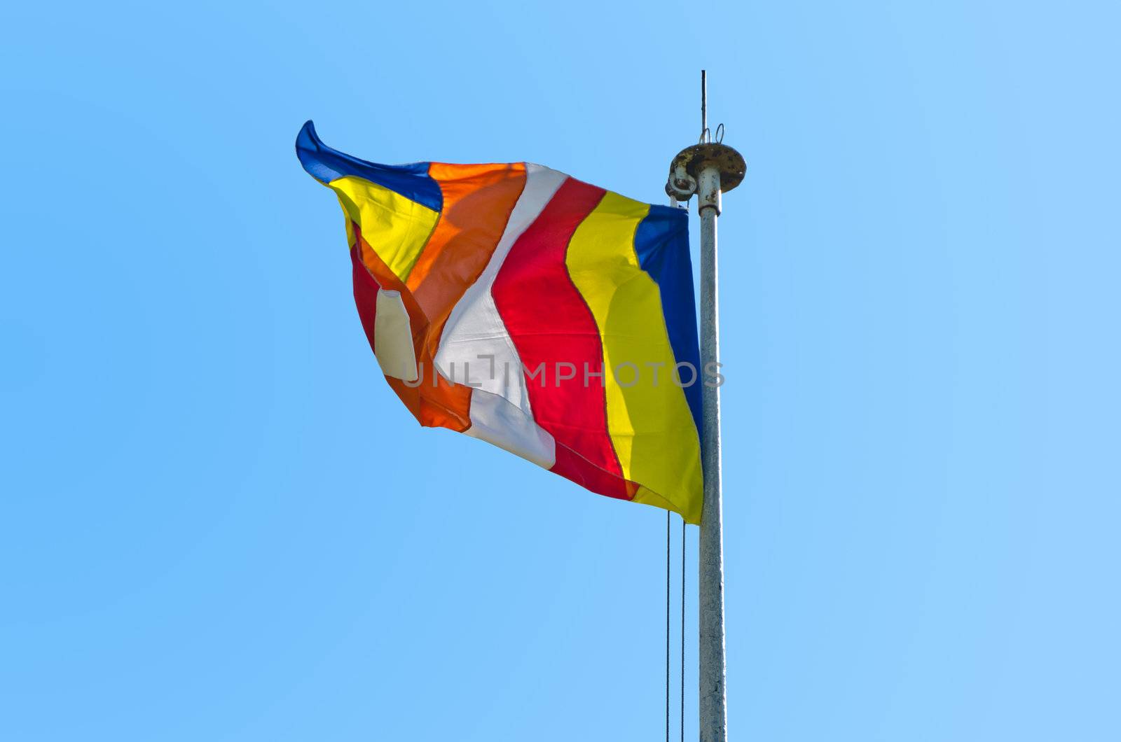 symbolic flag of Buddhism against the cloudless sky. The six vertical bands of the flag represent the six colors of the aura which Buddhists believe emanated from the body of the Buddha when he attained enlightenment