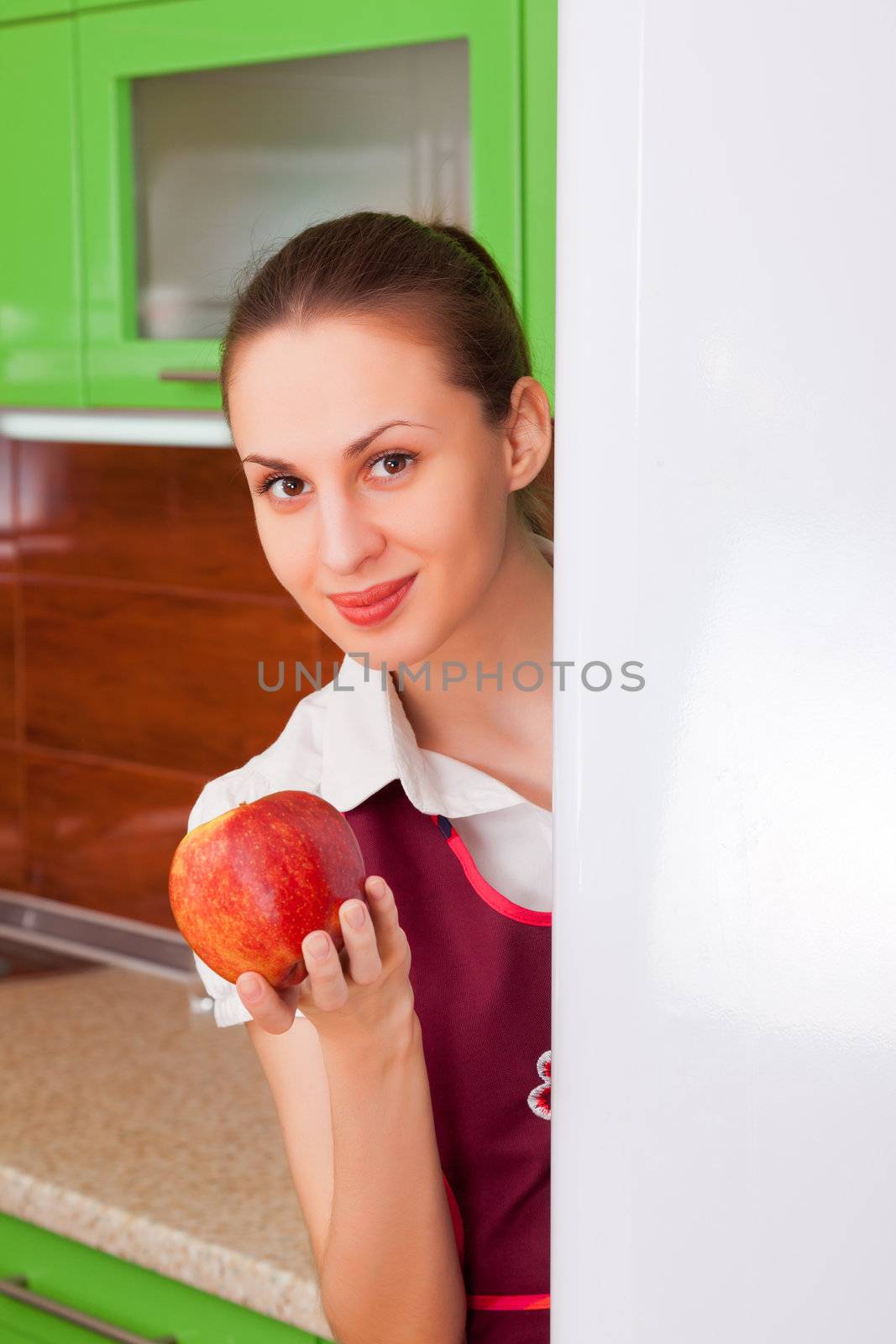 young housewife holding a ripe apple on the background of the kitchen