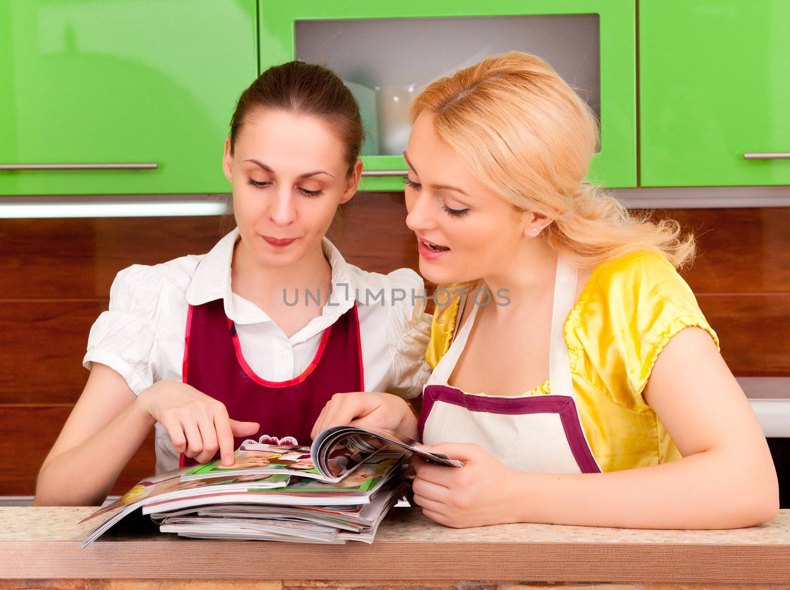 Two young women discuss fashion magazines in the kitchen