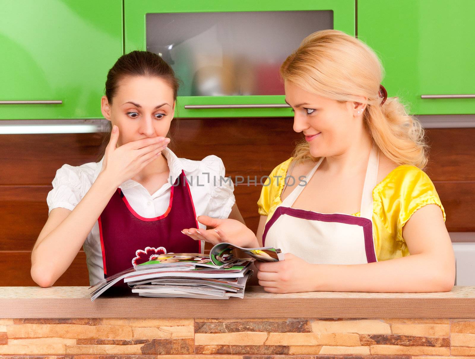 Two young women discuss fashion magazines in the kitchen
