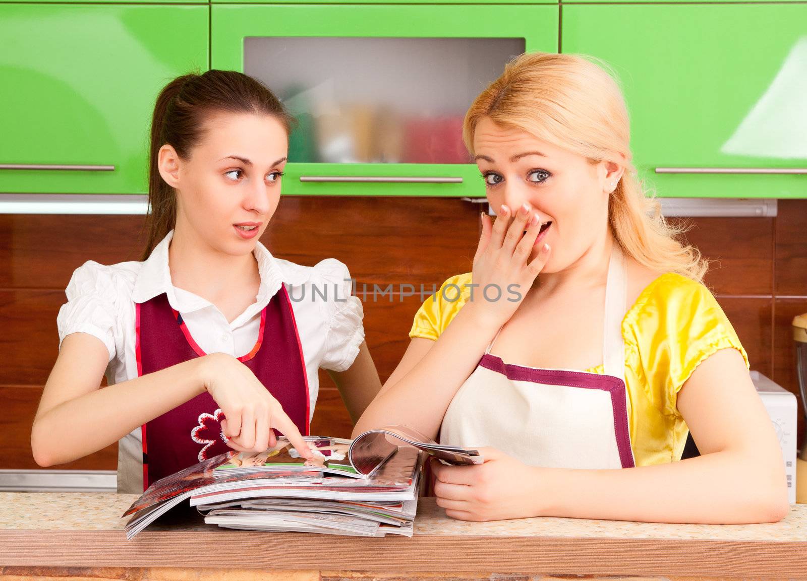 Two young women discuss fashion magazines in the kitchen