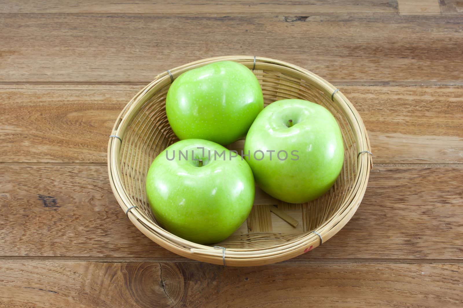 3 green apples on basket with teak wood background.