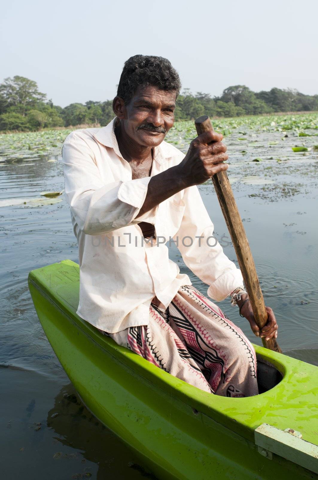 Habarane, Sri Lanka - December 04, 2011: Smiling Sri Lankian man are floating by small traditional green boat upon a lake.
