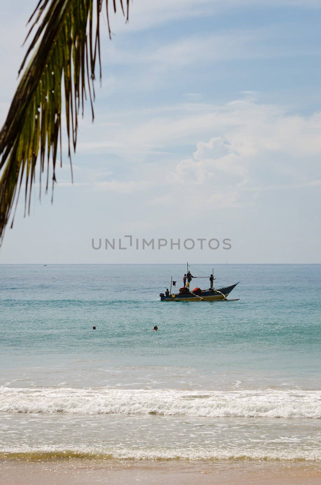 Mirissa, Sri Lanka - December 12, 2011: Traditional Asian small motorboat with four fishermen and fishing net with a palm leaf and beach on front.