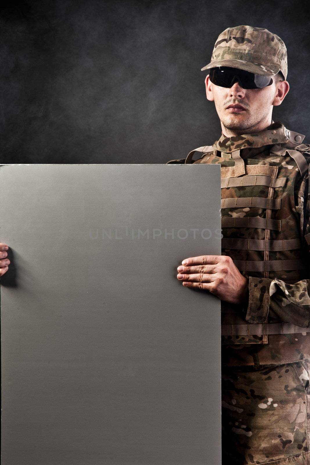 Modern soldier is holding a poster with smoke isolarted on black background