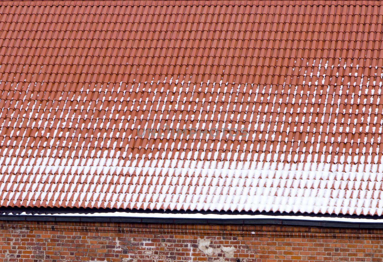 Snowy clay tile roof and red brick wall background in winter.