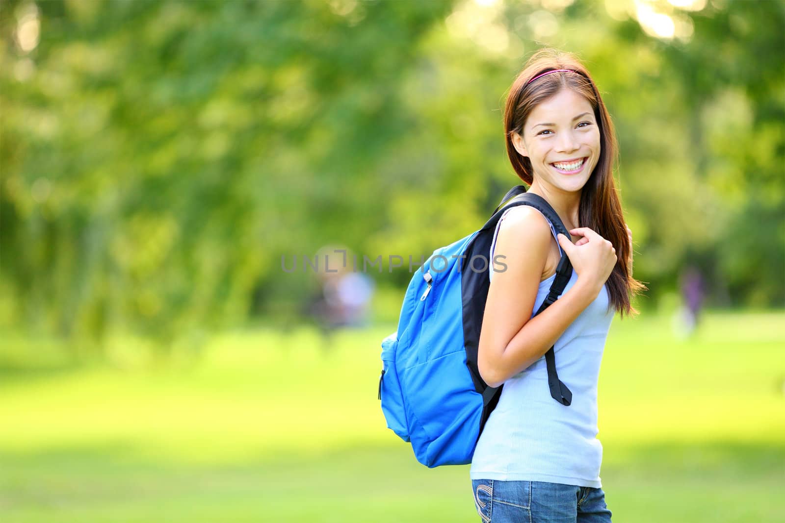 Girl student in summer / spring park standing with backpack or school bag smiling happy. Portrait of young Asian female university student - mixed race Asian Chinese / Caucasian woman.