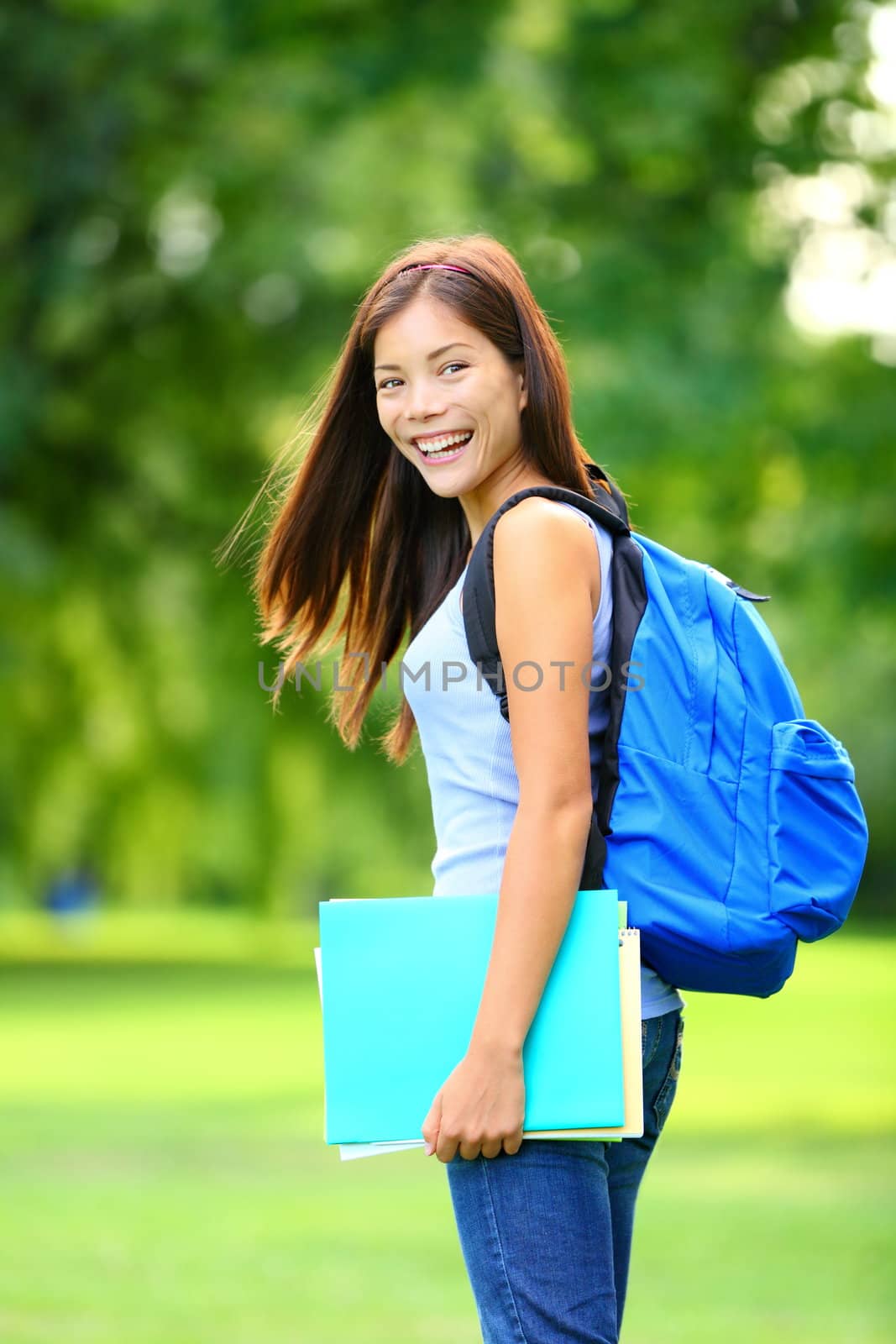 University / college student girl standing happy smiling with book or notebook in campus park. Beautiful young mixed race Asian / Caucasian young woman brunette.