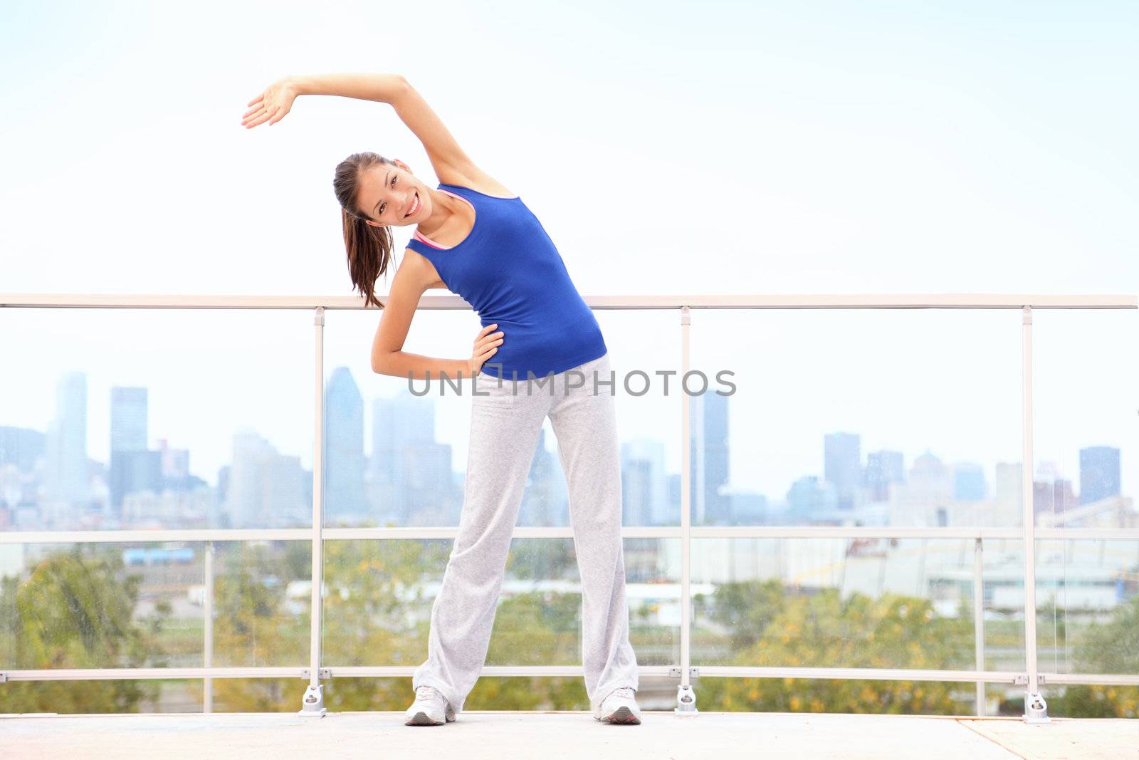 City workout woman stretching after running exercise with skyline in background. Young fitness model training. Mixed race Asian Chinese / Cauasian young woman in Montreal, Quebec, Canada.