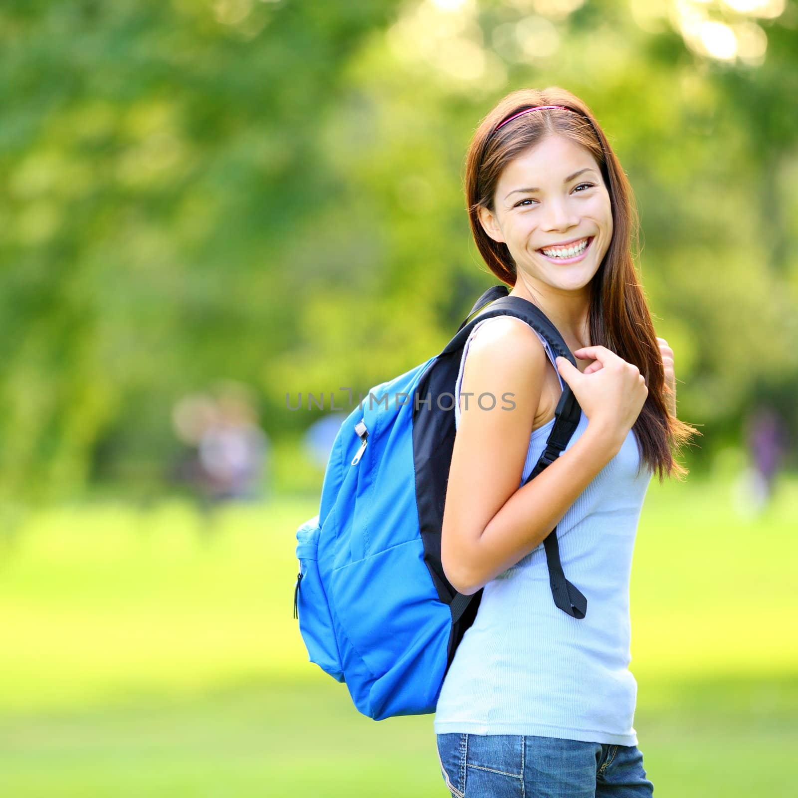 Student girl outside in summer park smiling happy. Asian female college or university student. Mixed race Asian / Caucasian young woman model wearing school bag.