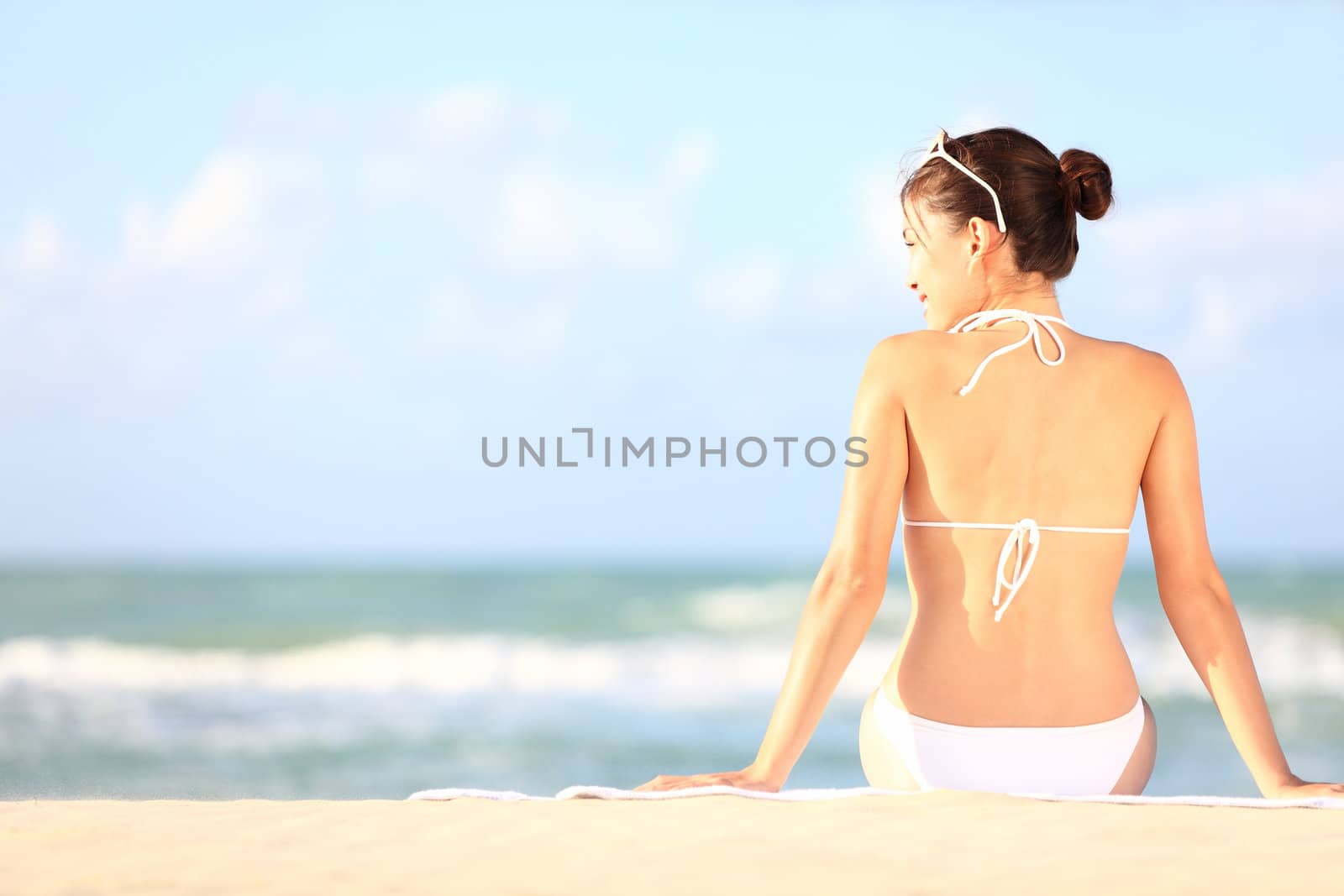 Beach holidays woman enjoying summer sun sitting in sand looking happy at copy space. Beautiful young bikini model. Mixed race Caucasian / Asian Chinese.