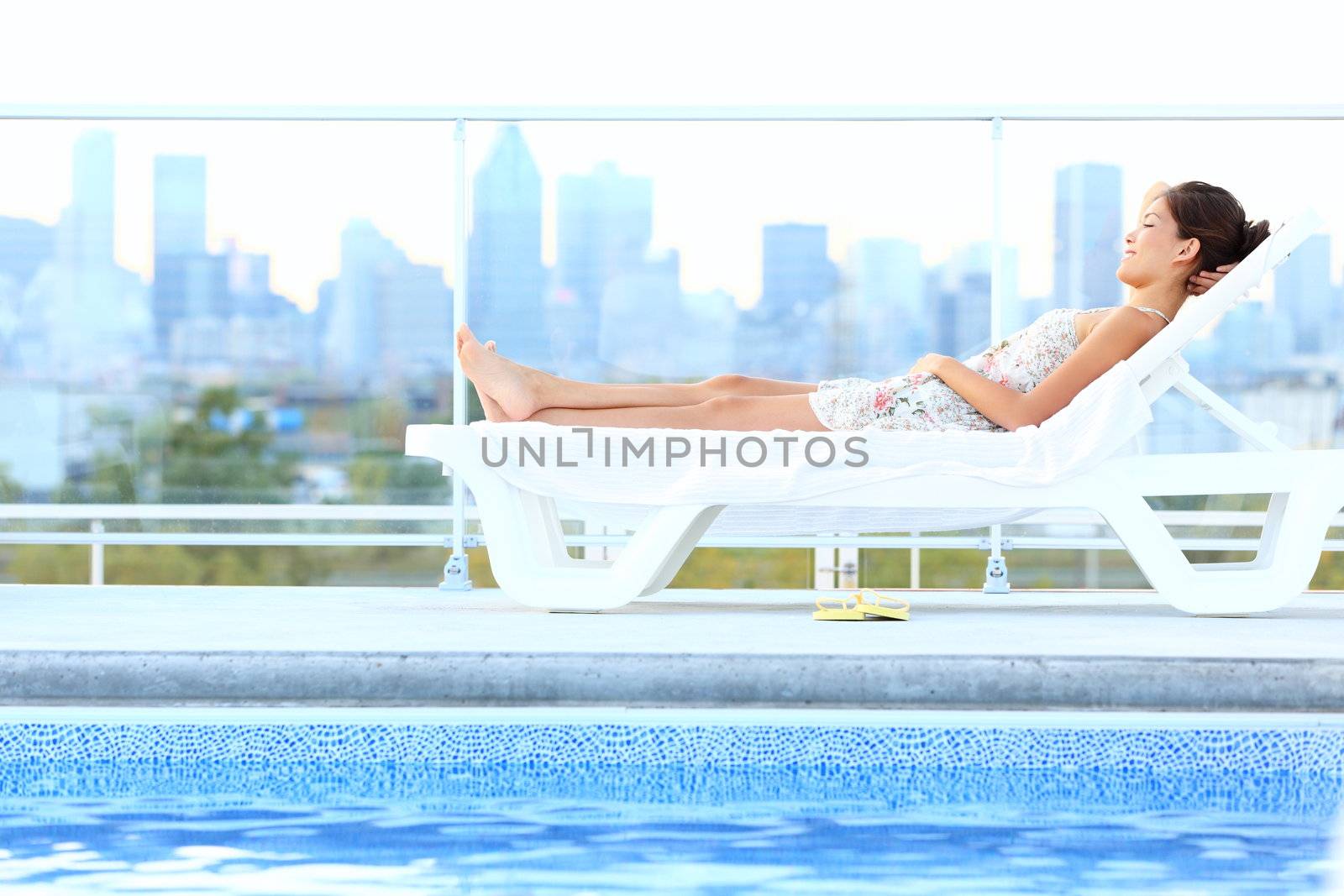 Urban luxury city lifestyle woman lying by pool relaxing in sun lounger during summer in Montreal, Quebec, Canada.