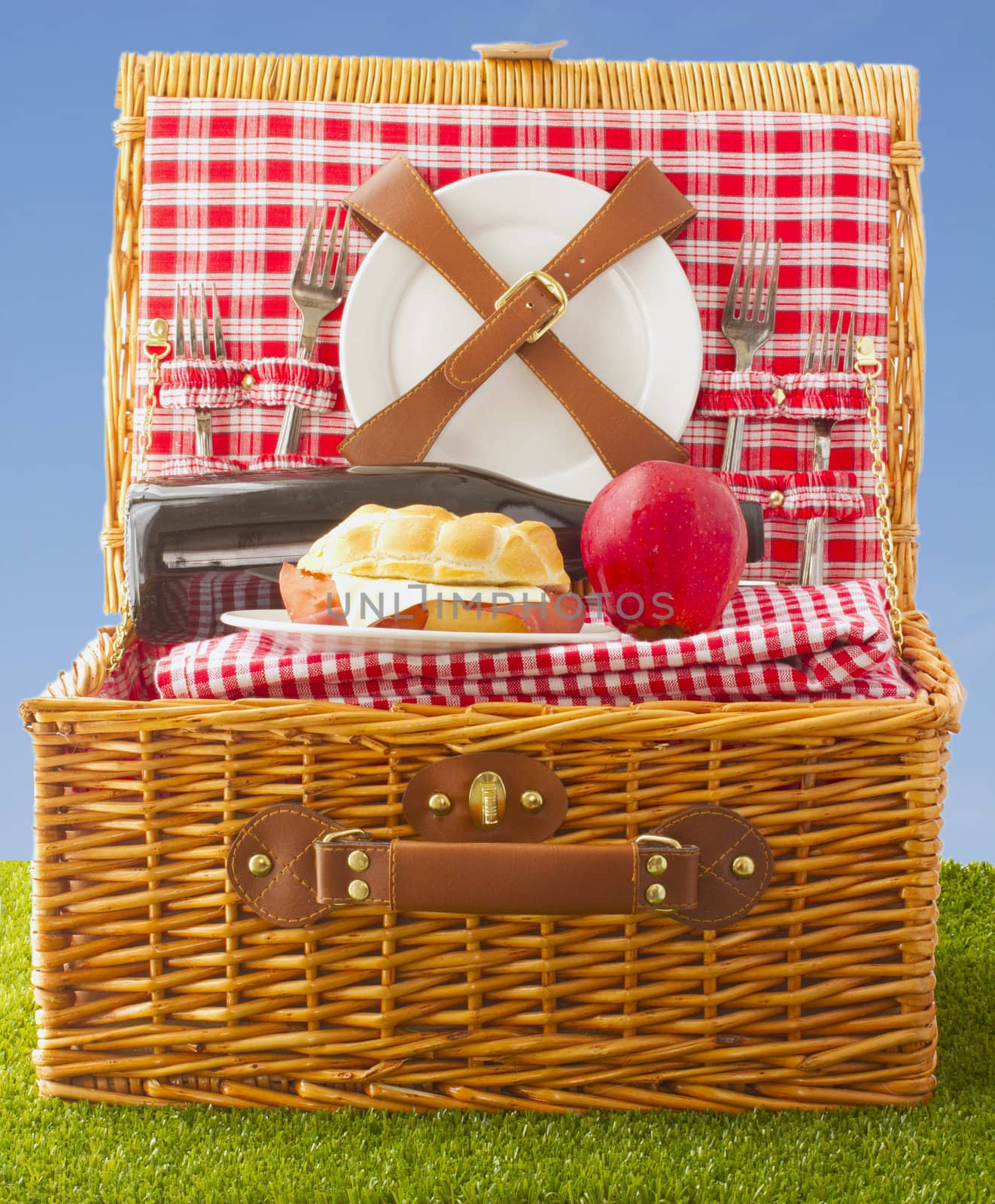 Wooden basket for picnic with sandwich, wine and apple over a grass field