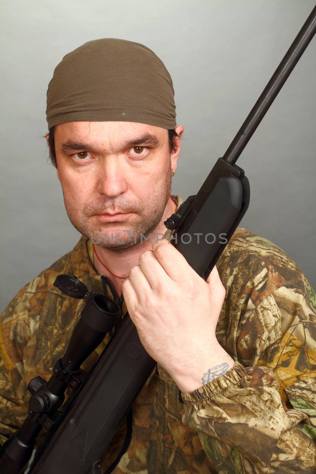 the man in a camouflage with a rifle in hands looks in a chamber lens.