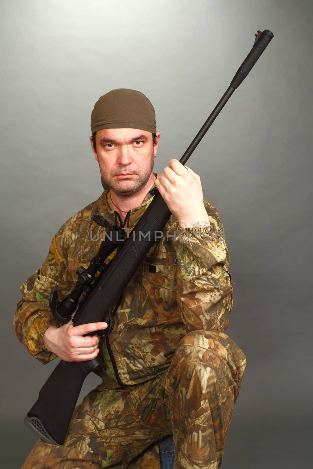 the man in a camouflage with a rifle in hands costs on one knee and looks in a chamber lens