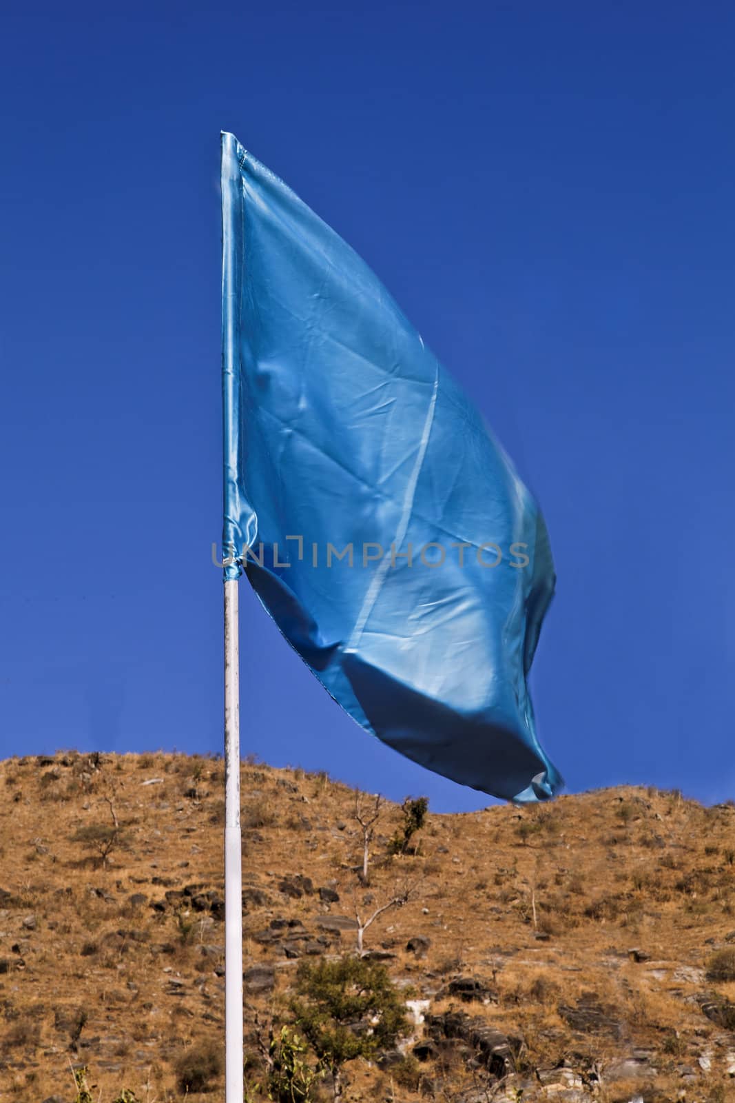 Portrait of a vertical flagpole with a silky blue turquoise flag waving in the breeze
