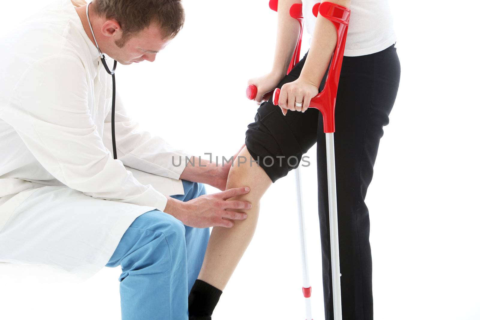 Orthopaedic surgeon sitting examining the knee of a female patient on crutches following surgery for a joint injury