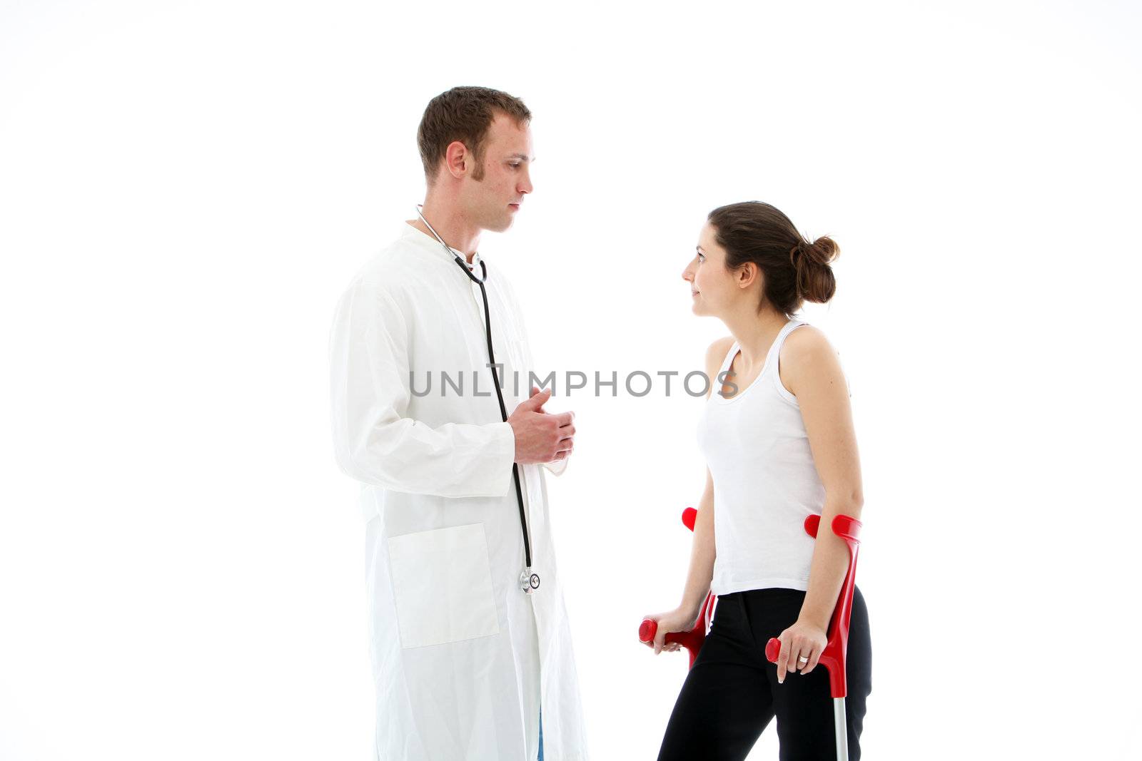 Earnest young doctor standing talking to female patient on crutches during a post operative consultation in his surgery