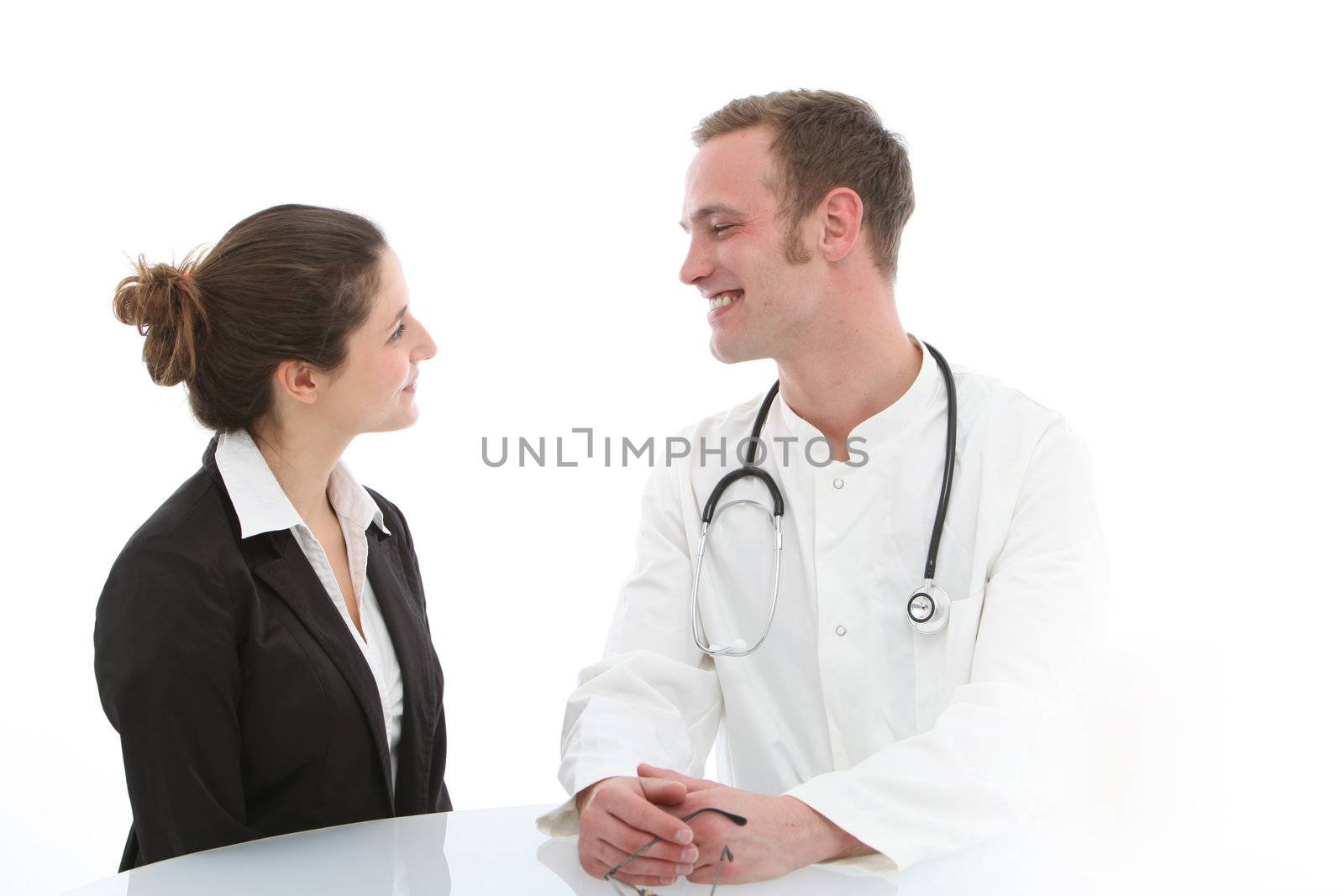 Smiling young male doctor seated at a table giving good news to his female patient during a consultation