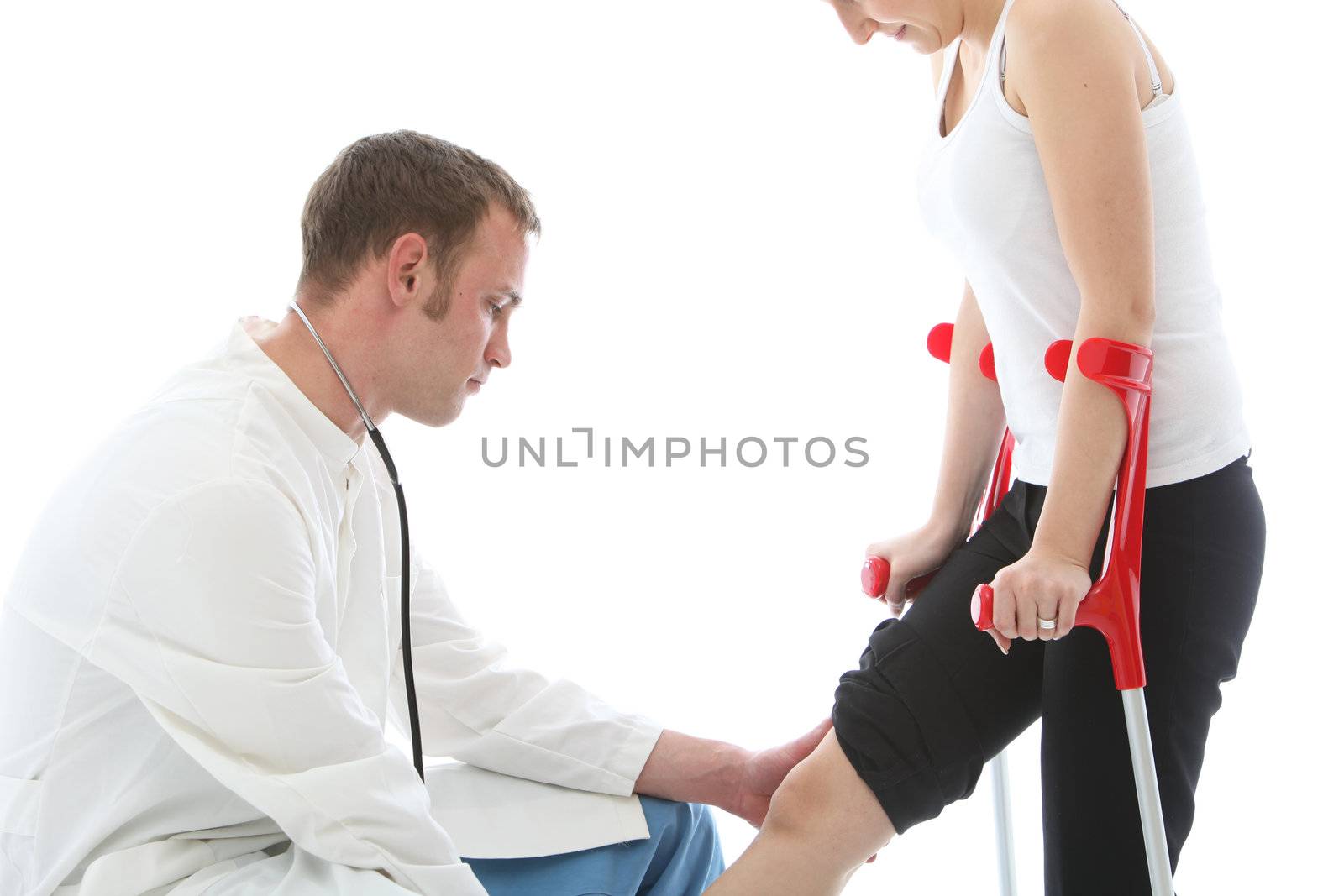 Orthopaedic surgeon kneeling down examining the knee joint of a female patient on crutches isolated on white