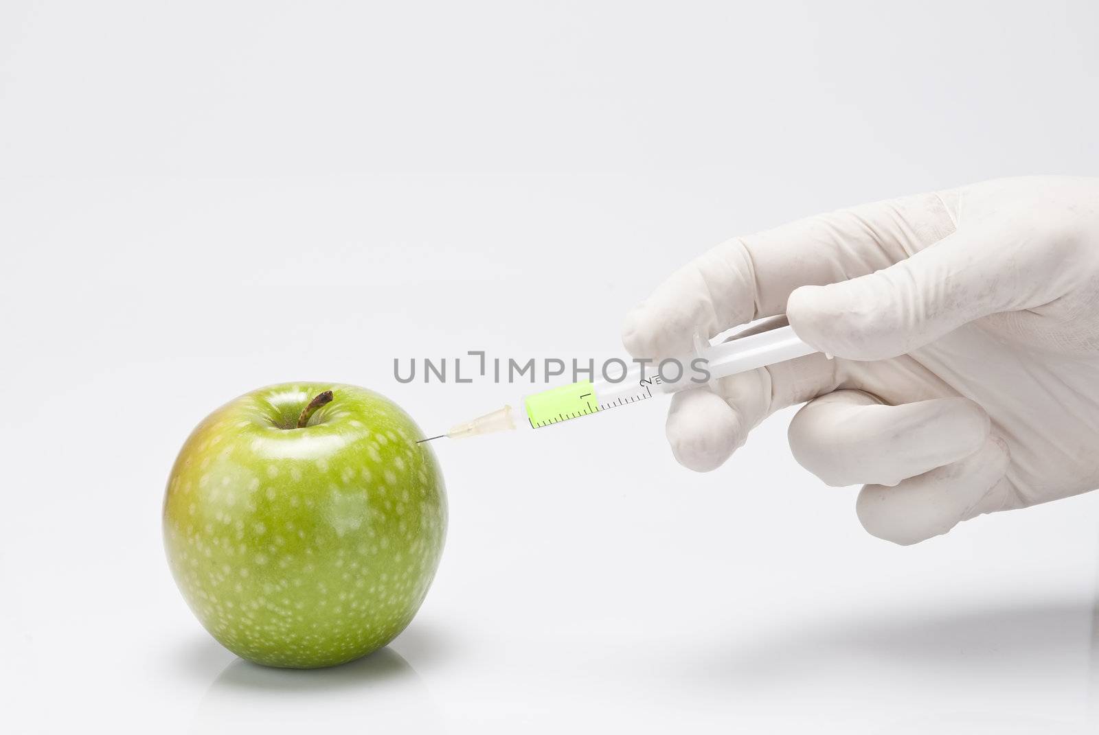 A gloved hand injecting an apple with a syringe on a white background.