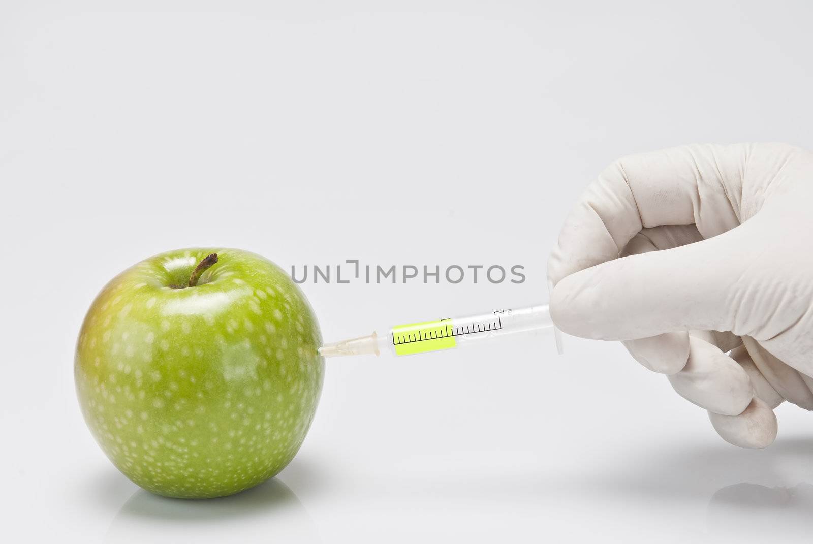 A gloved hand injecting an apple with a syringe on a white background.