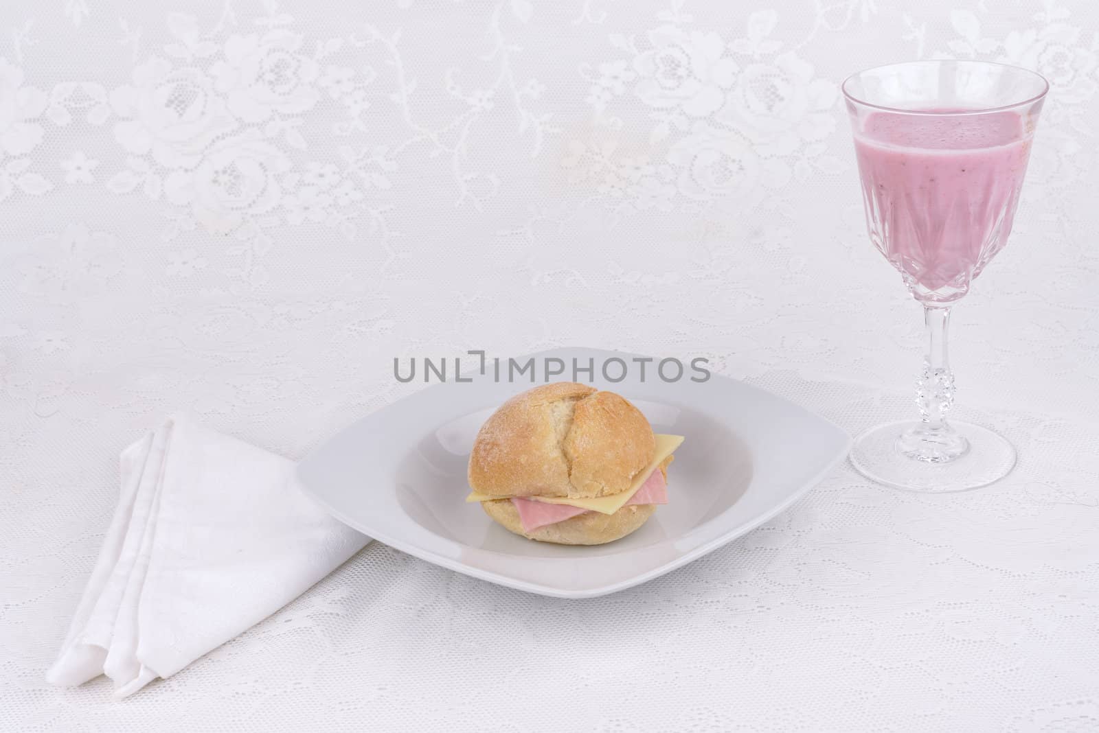 Strawberry shake in a glass and a bread with ham and cheese on a plate.