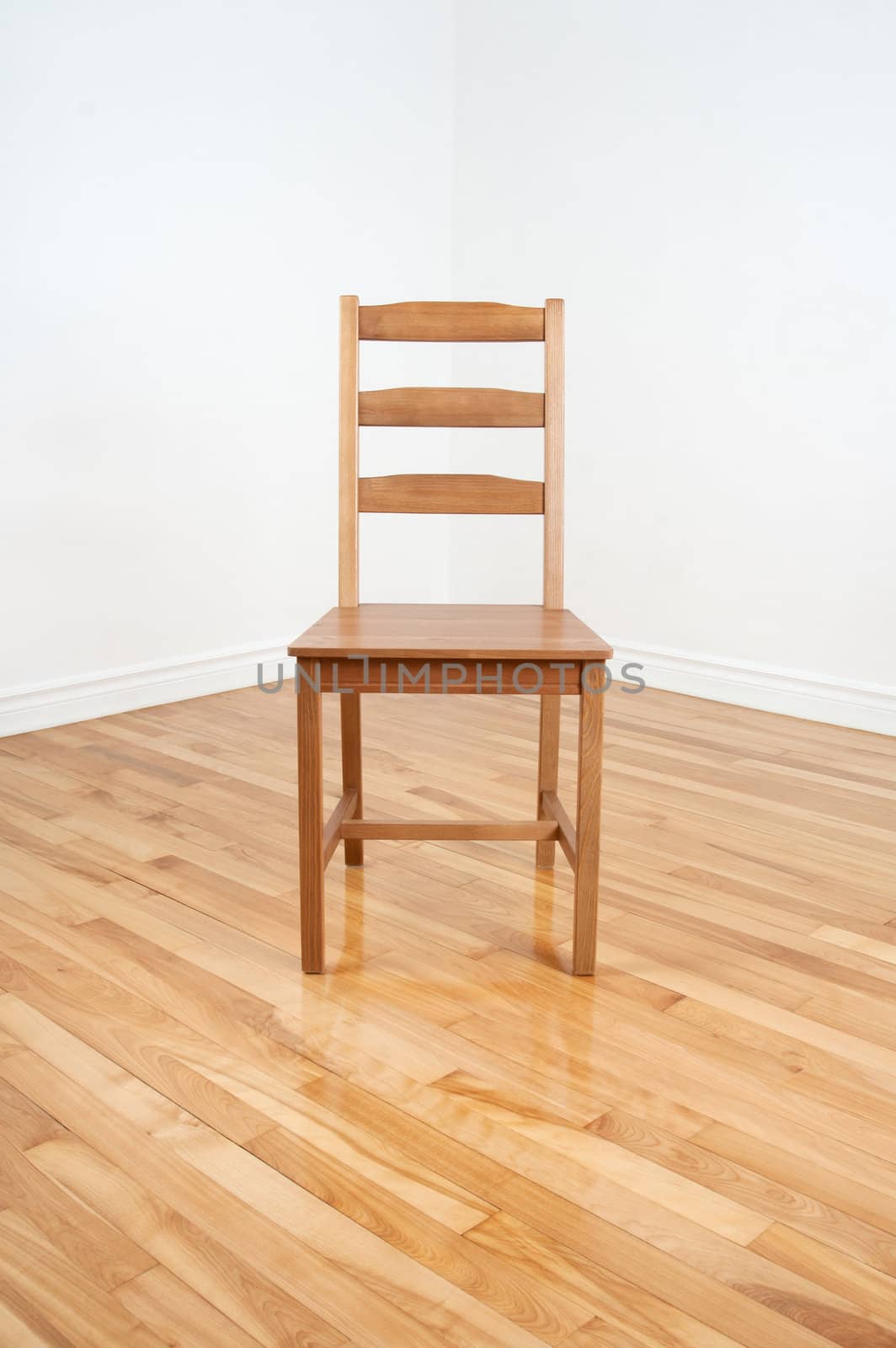 Wooden chair in the empty corner of a room with white walls and wooden floor.