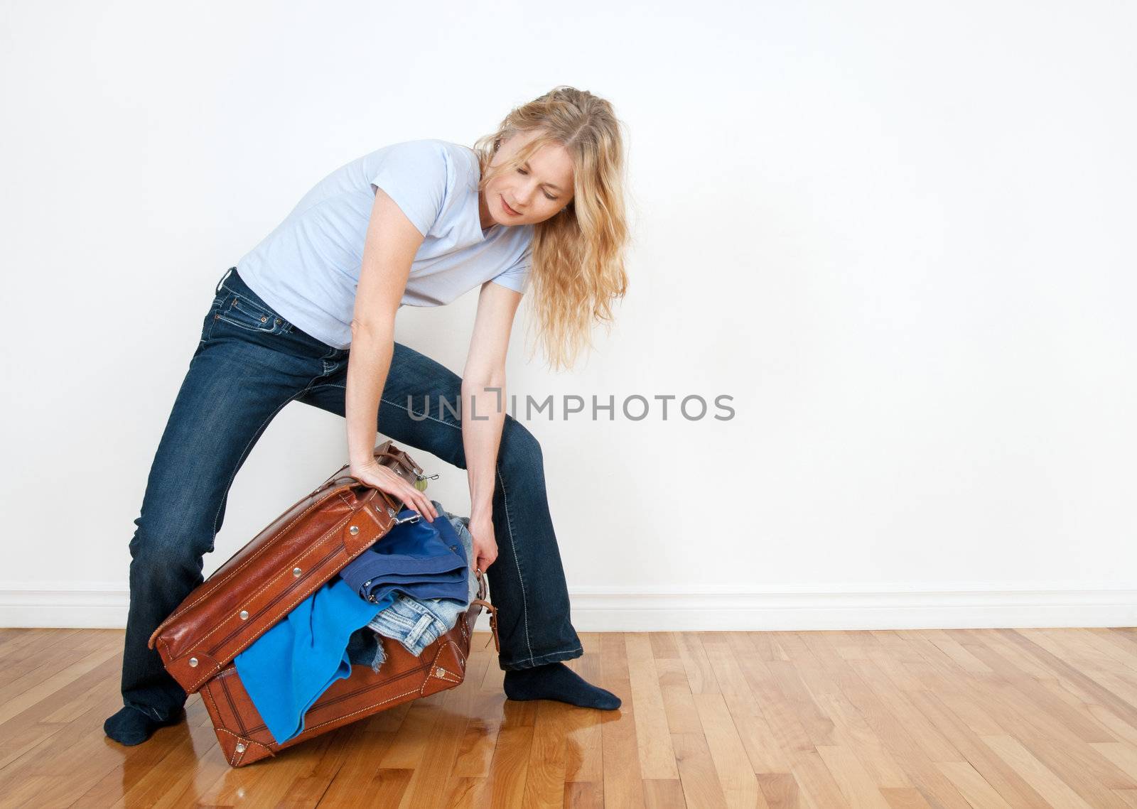 Young woman tries to close a suitcase with too much clothing in it.