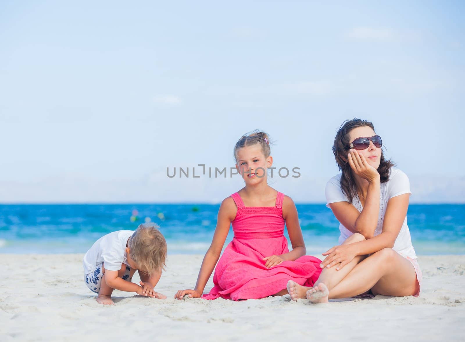 Happy family of three sitting and having fun on tropical beach