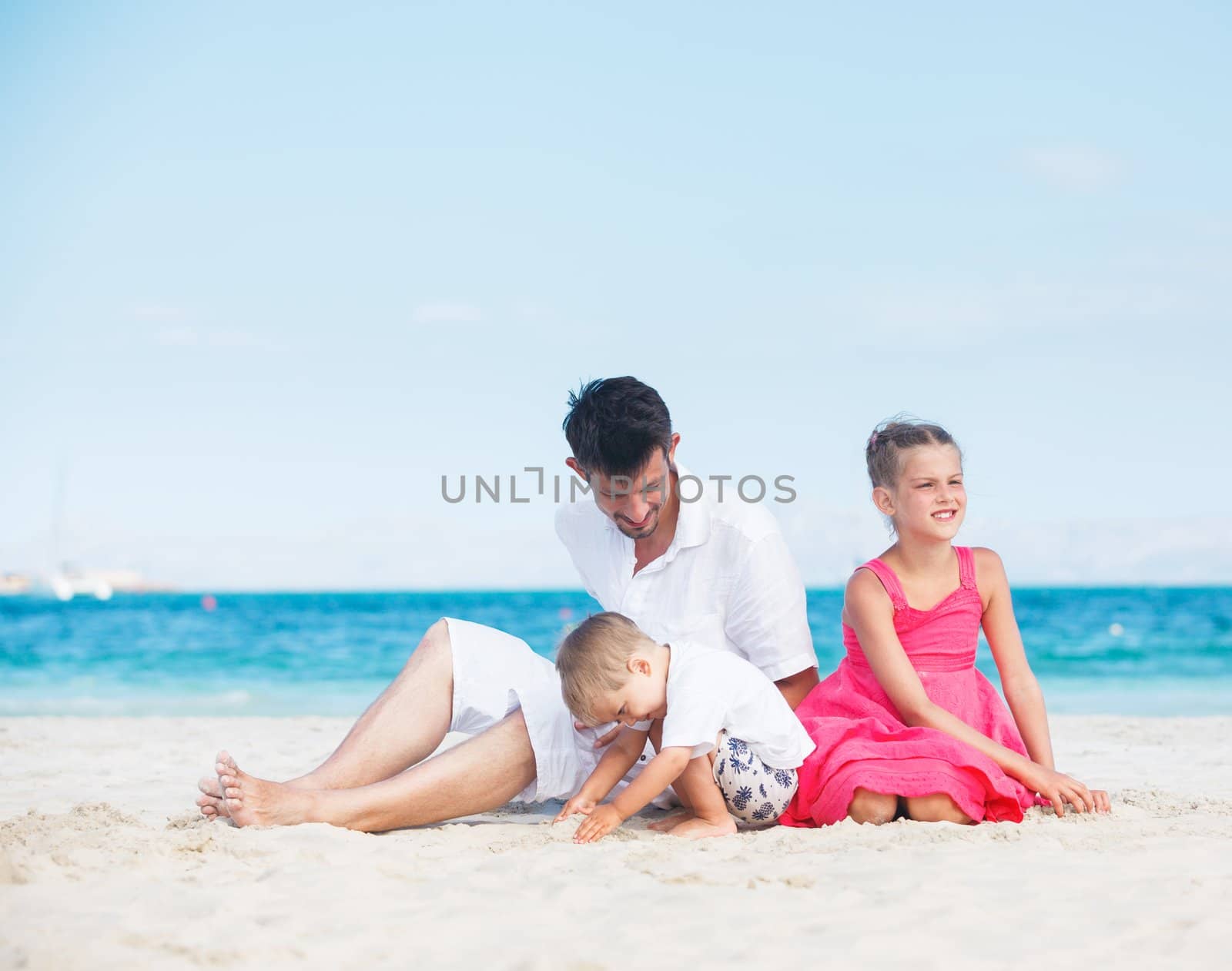 Happy family of three sitting and having fun on tropical beach