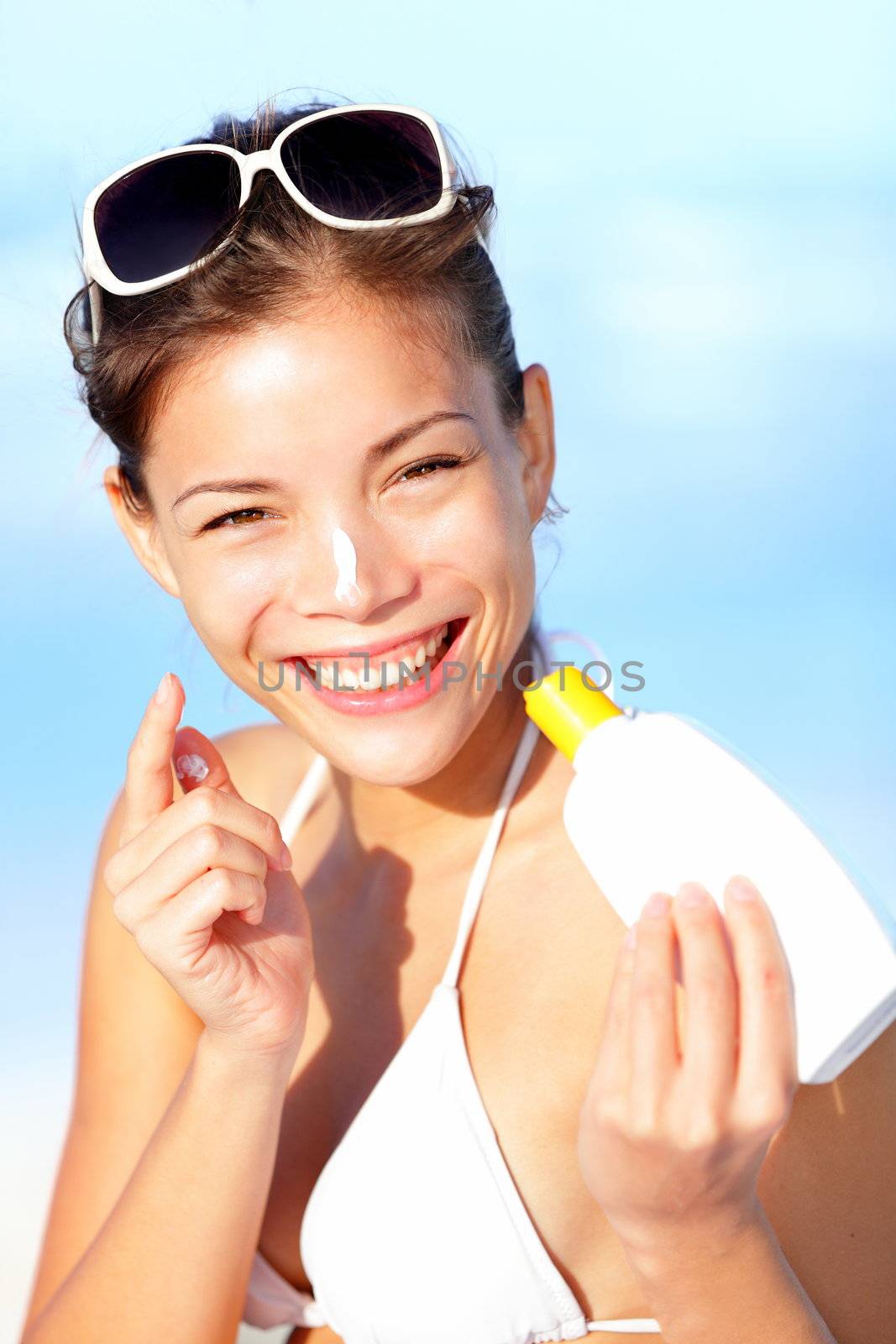 Vacation woman putting sunscreen on nose on beach. Cute beautiful young woman on summer holiday enjoying the sun on sunny summer day. Multiracial Asian / Caucasian girl.