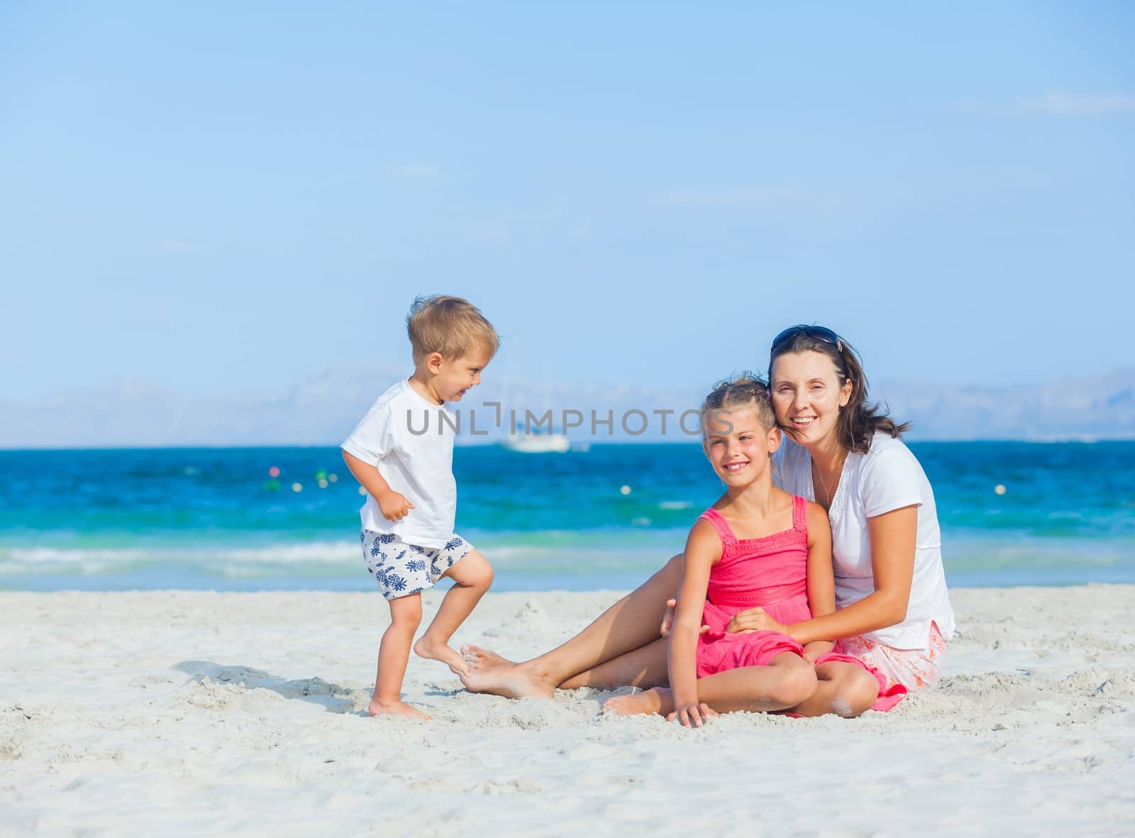 Happy family of three sitting and having fun on tropical beach