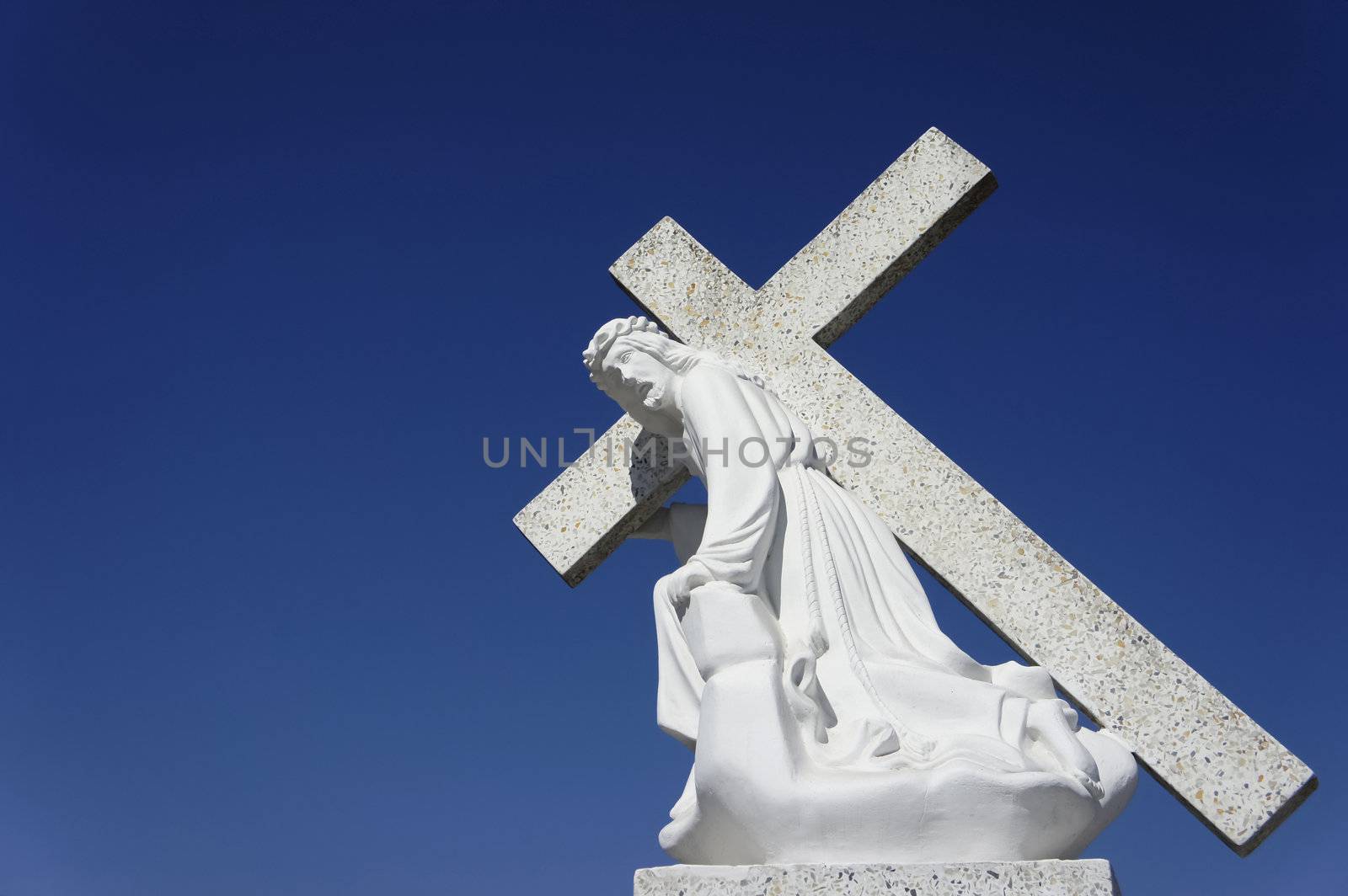 A statue of Jesus carrying the cross on blue sky background.