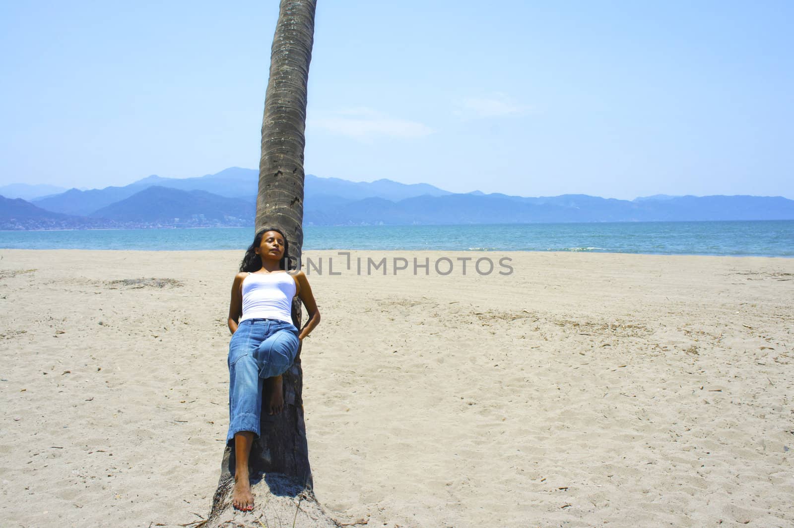 Young latina woman leaning on a palm tree. 