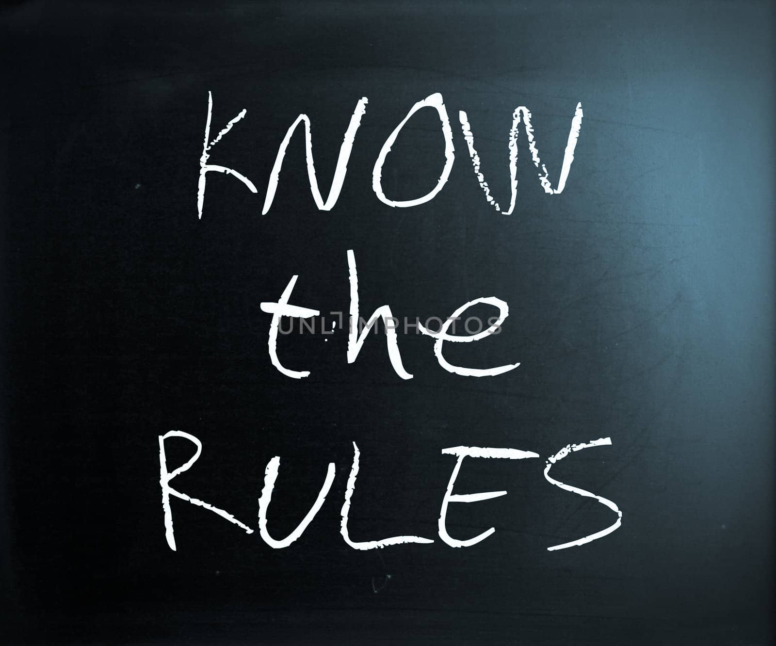 "Know the rules" handwritten with white chalk on a blackboard.