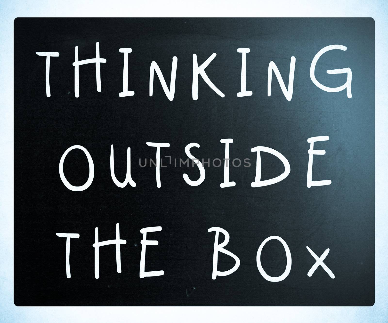 Thinking outside the box phrase, handwritten with white chalk on a blackboard