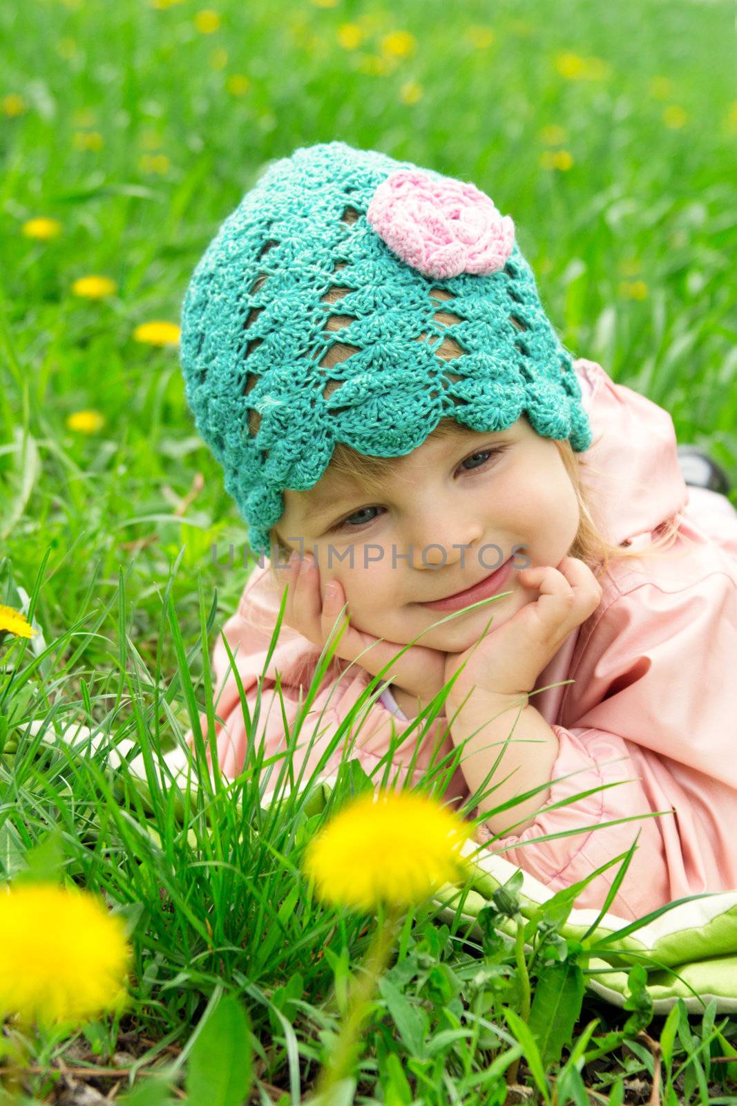 Smiling baby girl lying among field of dandelions