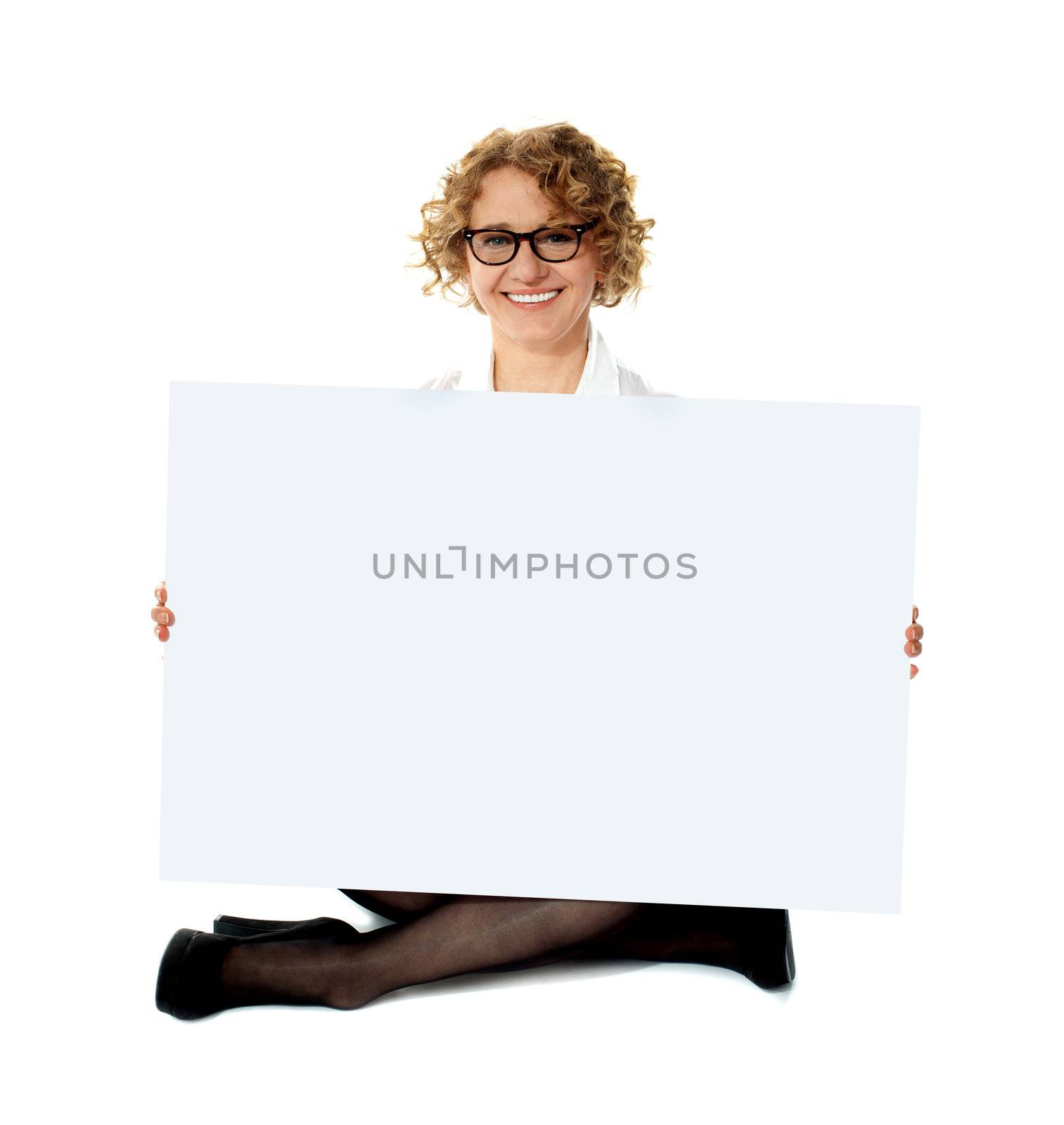 Female employee holding white blank banner ad seated on floor, legs-crossed