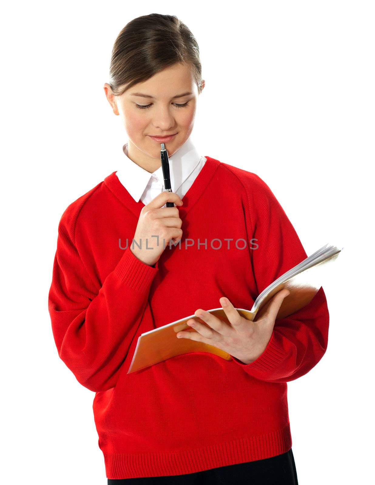 Cute school girl thinking and looking into notebook. Isolated over white