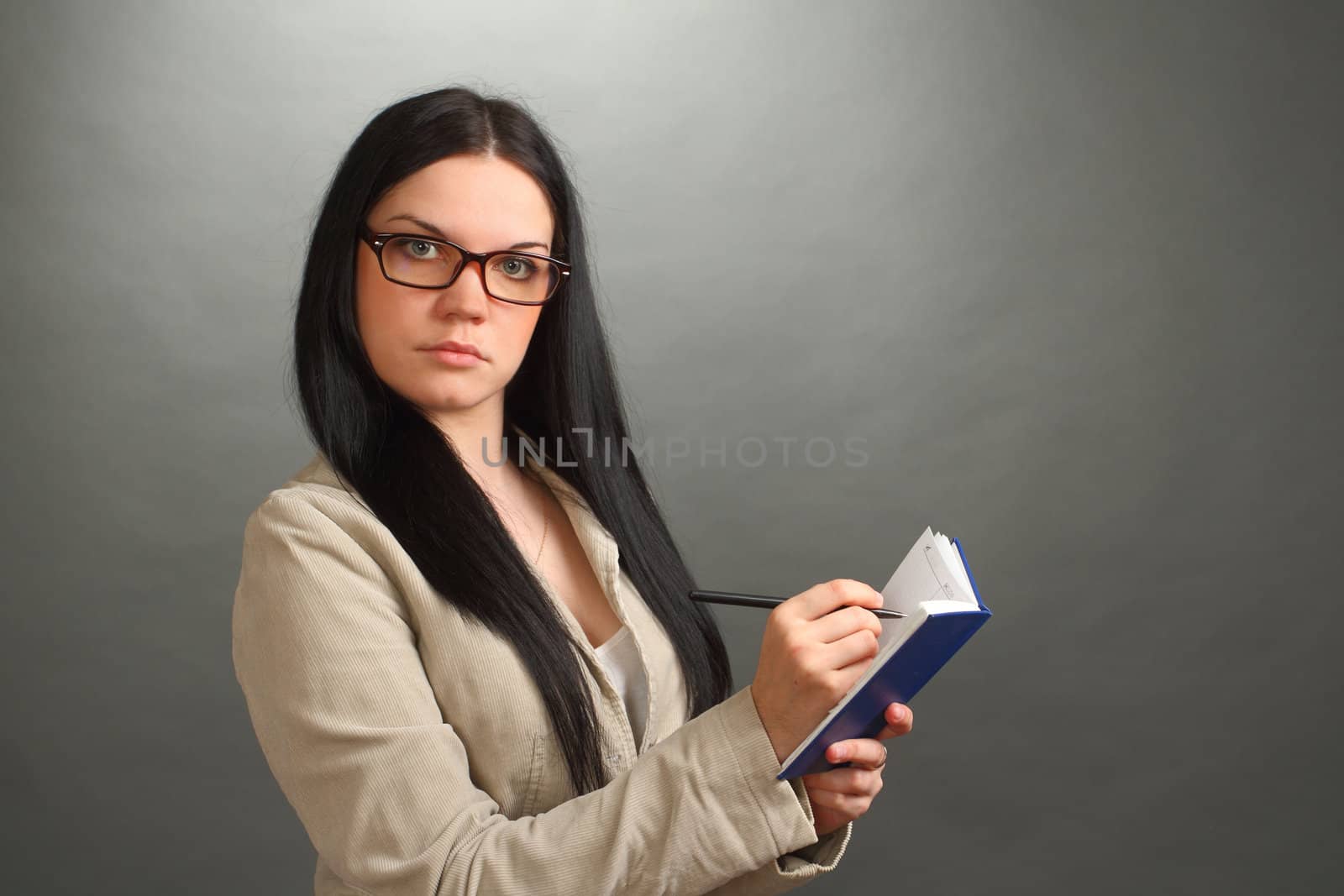 the serious girl, the brunette wearing spectacles with the handle and a notebook on a gray background