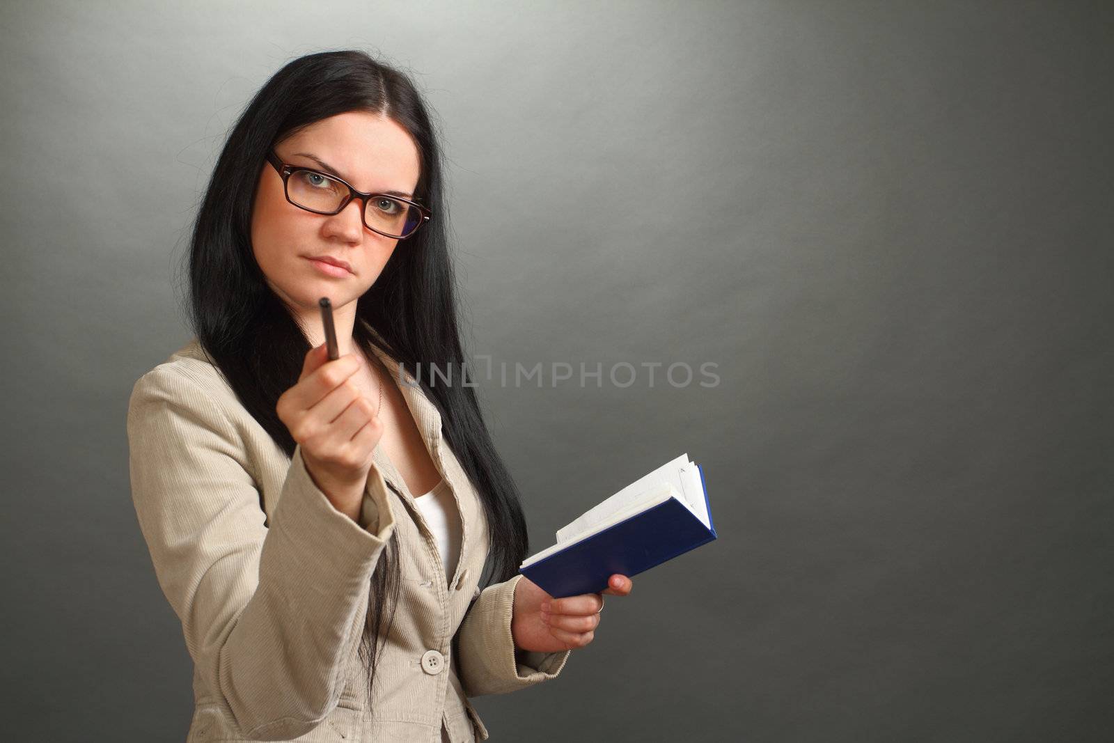 the serious girl, the brunette wearing spectacles with the handle and a notebook on a gray background, looks in the chamber