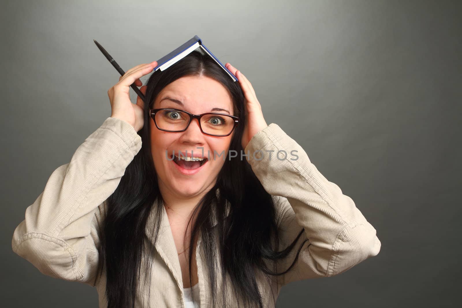 the girl, the brunette wearing spectacles with a notebook on the head, on a gray background, looks in the chamber, panics, a double 2