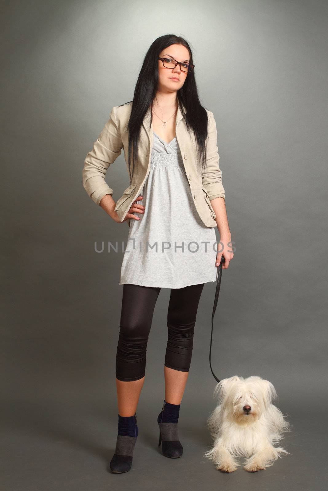 The beautiful serious 
the brunette wearing spectacles with a white shaggy doggie on a gray background, looks in the chamber