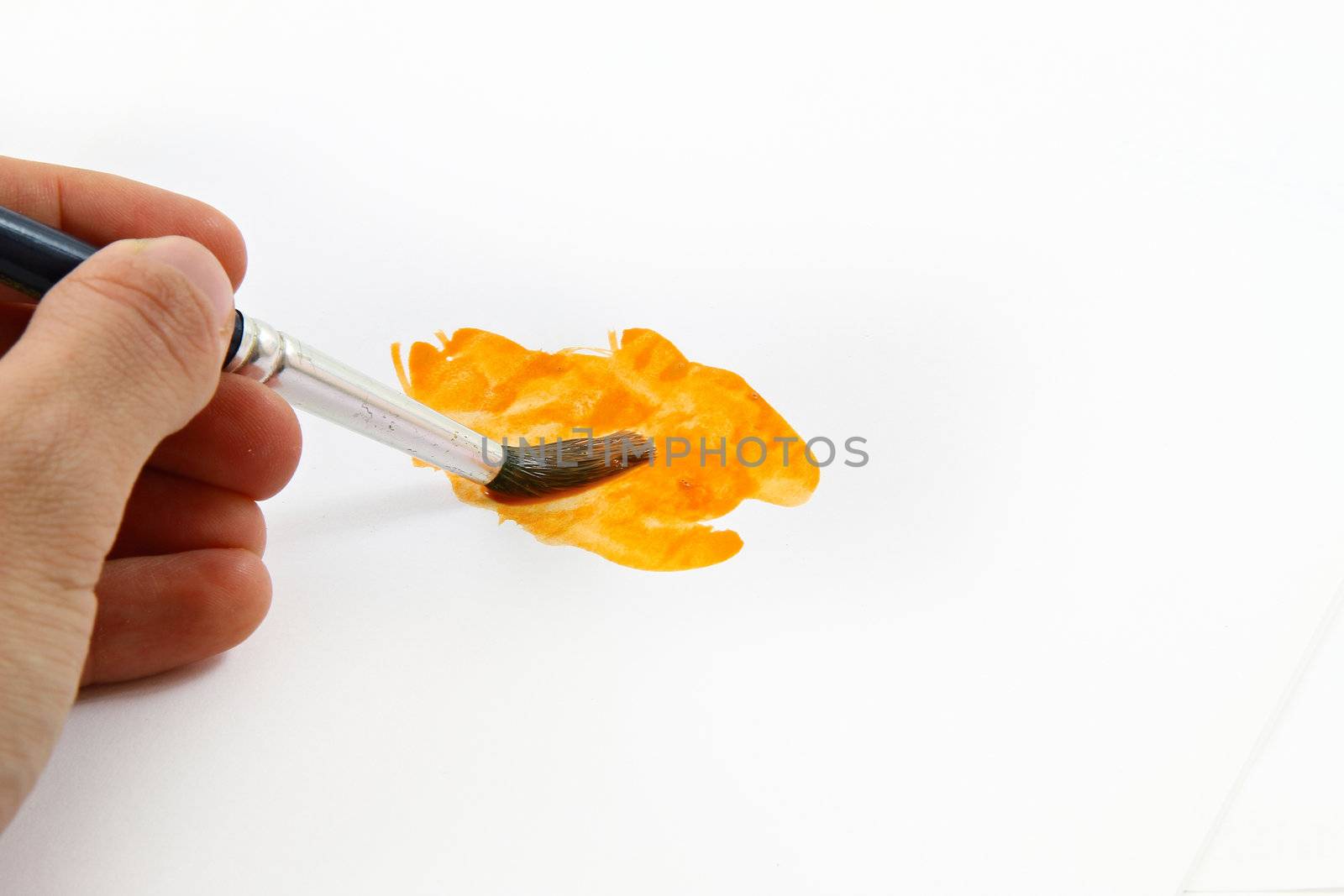 Painter holding a thick brush and painting orange abstract shape on a white paper