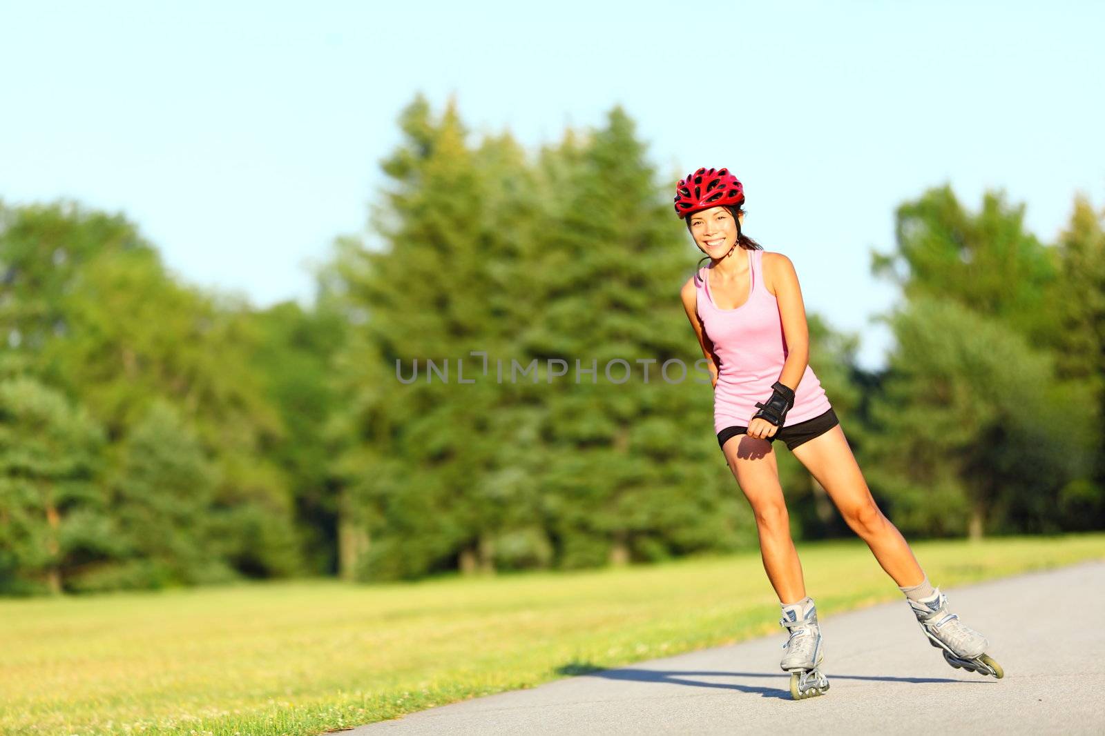 Skating woman on rollerblades in park. Girl going rollerblading sitting in grass putting on inline skates. Mixed race Asian Chinese / Caucasian woman in outdoor activities.