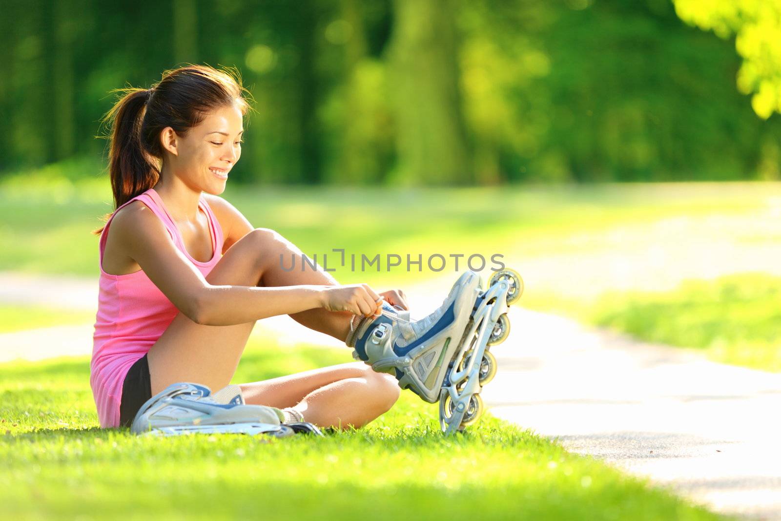 Woman skating in park. Girl going rollerblading sitting in grass putting on inline skates. Mixed race Asian Chinese / Caucasian woman in outdoor activities.