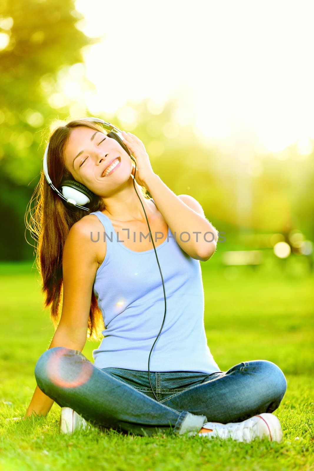 Woman listening to music. Female student girl outside in park listening to music on headphones while studying. Happy young university student of mixed Asian and Caucasian ethnicity.