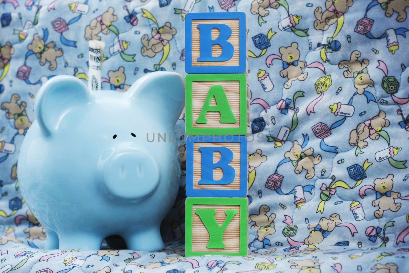 Wooden blocks spell "Baby" next to a blue piggy bank over a baby blanket
